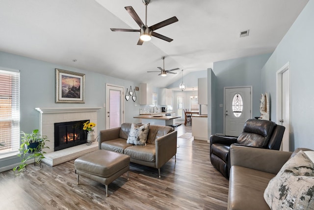 living room with visible vents, a ceiling fan, wood finished floors, a brick fireplace, and vaulted ceiling