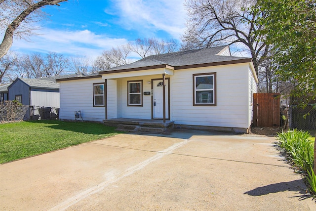 view of front of house with concrete driveway, a front lawn, roof with shingles, and fence