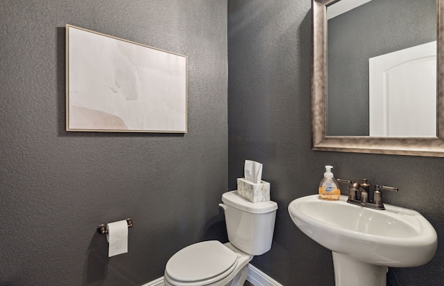 bathroom featuring a textured wall, toilet, a sink, and baseboards