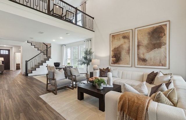 living area with recessed lighting, wood finished floors, a towering ceiling, baseboards, and stairs