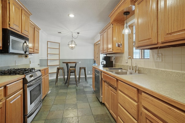 kitchen featuring a wainscoted wall, hanging light fixtures, stainless steel appliances, light countertops, and a sink