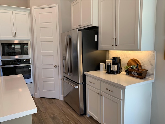 kitchen with stainless steel appliances, white cabinetry, light countertops, decorative backsplash, and dark wood-style floors