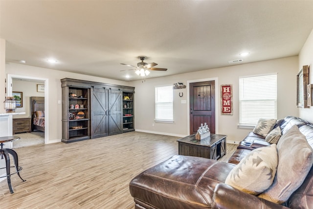 living room with ceiling fan, a barn door, visible vents, baseboards, and light wood-type flooring