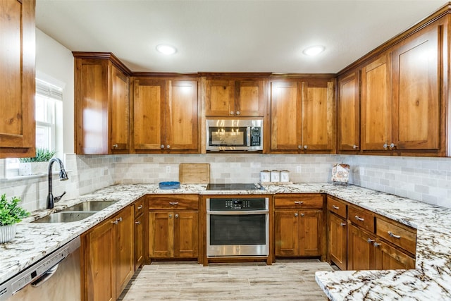 kitchen featuring appliances with stainless steel finishes, a sink, light stone countertops, and brown cabinets