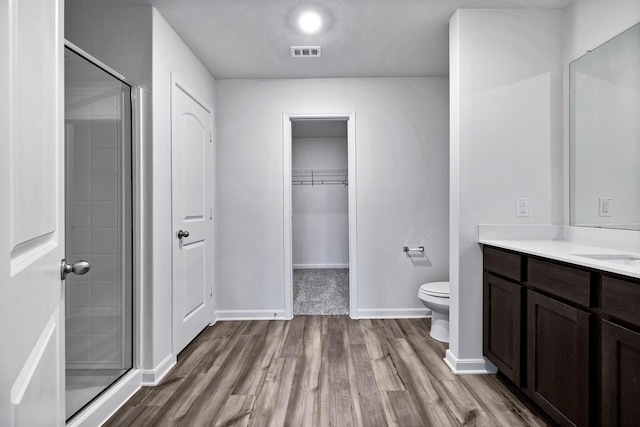 full bath featuring a walk in closet, visible vents, toilet, a stall shower, and wood finished floors