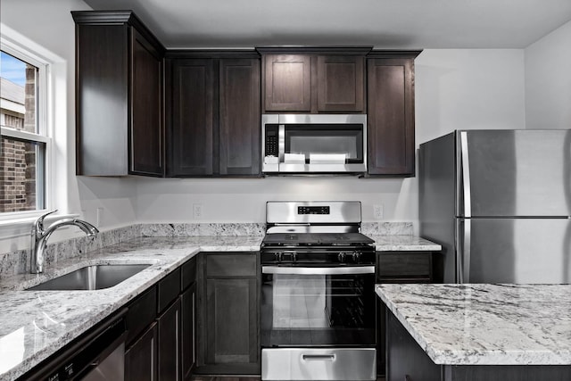 kitchen with stainless steel appliances, a sink, dark brown cabinets, and light stone countertops