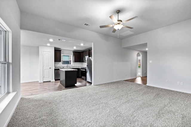 unfurnished living room with carpet floors, arched walkways, visible vents, and ceiling fan