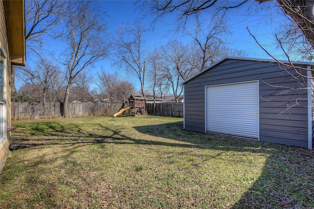 view of yard with an outbuilding, a playground, a fenced backyard, a detached garage, and driveway