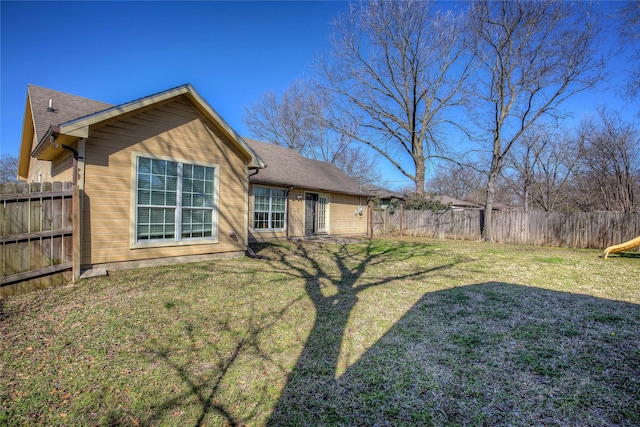 back of house featuring roof with shingles, a lawn, and fence private yard