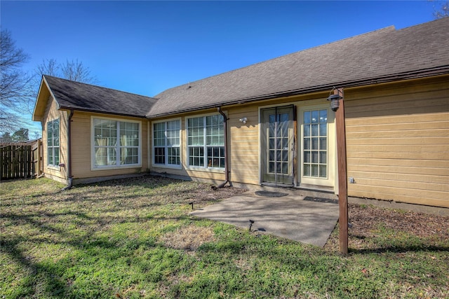 rear view of property featuring a patio area, fence, a lawn, and roof with shingles