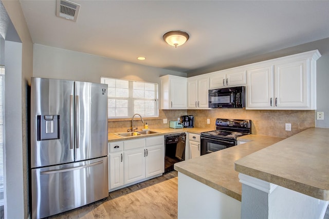 kitchen featuring light wood finished floors, visible vents, a peninsula, black appliances, and a sink