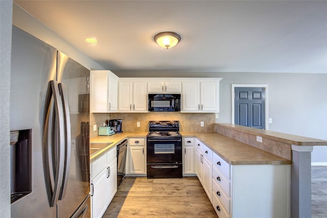 kitchen featuring a peninsula, black appliances, light wood-style flooring, and decorative backsplash