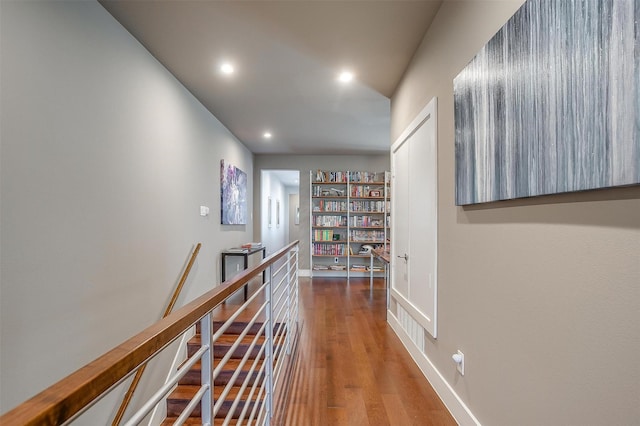 hallway featuring recessed lighting, baseboards, wood finished floors, and an upstairs landing