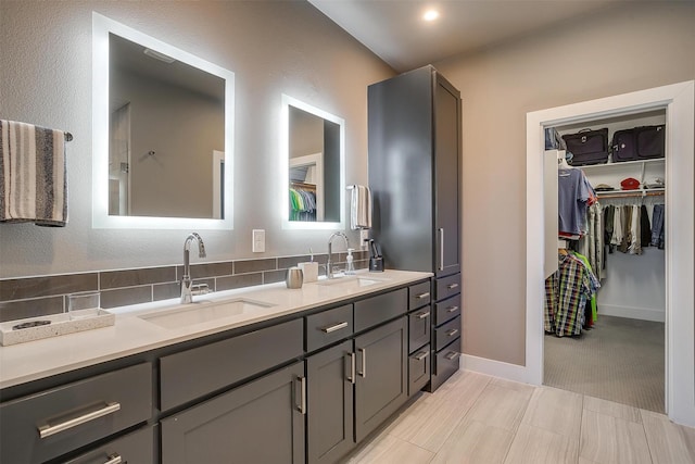 bathroom with double vanity, baseboards, a walk in closet, and a sink