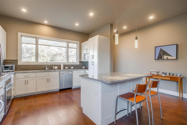 kitchen featuring white cabinets, a center island, hanging light fixtures, light stone countertops, and stainless steel appliances