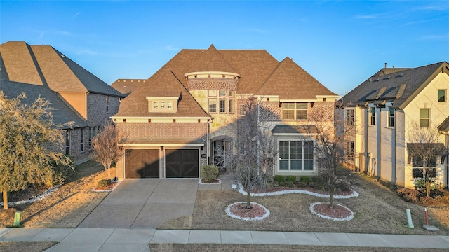 french provincial home featuring driveway, roof with shingles, a garage, and brick siding