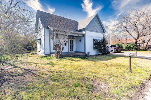 view of front of house featuring covered porch, roof with shingles, and a front yard