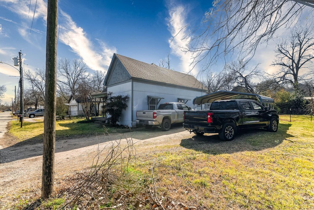 view of property exterior with dirt driveway, a yard, roof with shingles, and a detached carport