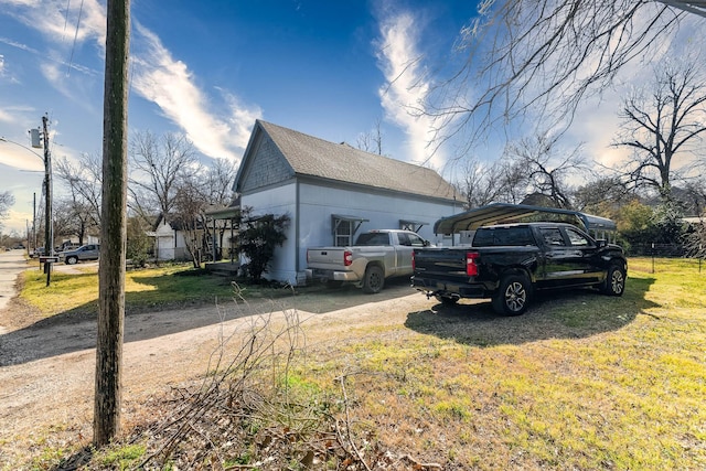 view of property exterior with dirt driveway, a yard, roof with shingles, and a detached carport