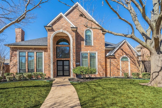 traditional home with a front yard, a chimney, and brick siding