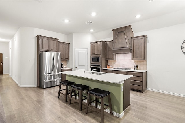 kitchen featuring a breakfast bar area, stainless steel appliances, light countertops, a center island with sink, and custom range hood