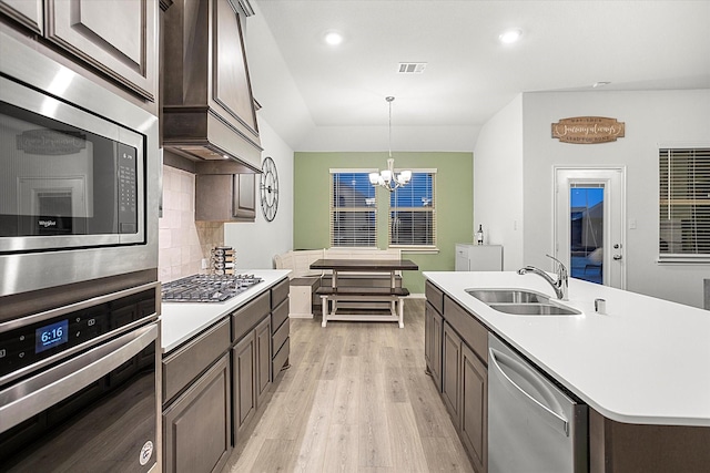 kitchen with a center island with sink, stainless steel appliances, light countertops, pendant lighting, and a sink