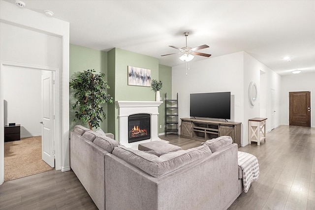 living area featuring a glass covered fireplace, ceiling fan, baseboards, and wood finished floors