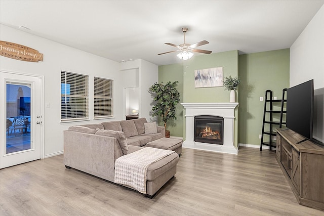 living room with light wood-style floors, a glass covered fireplace, baseboards, and a ceiling fan