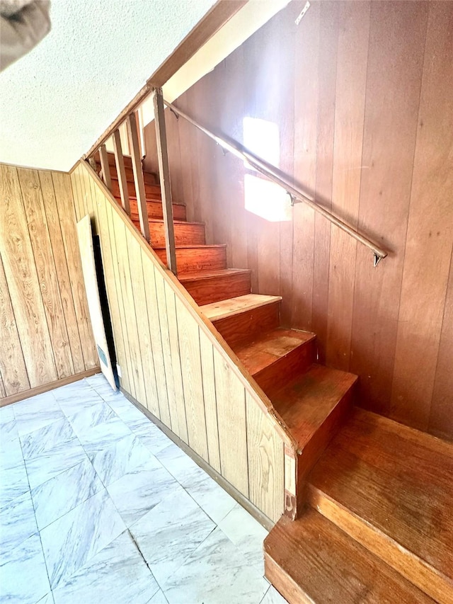 stairway featuring marble finish floor, a textured ceiling, and wood walls