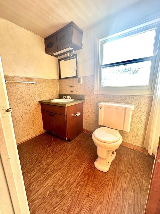 half bath with wainscoting, toilet, wallpapered walls, and wood finished floors