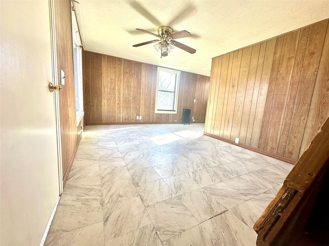 unfurnished room with a ceiling fan, wood walls, a textured ceiling, and baseboards