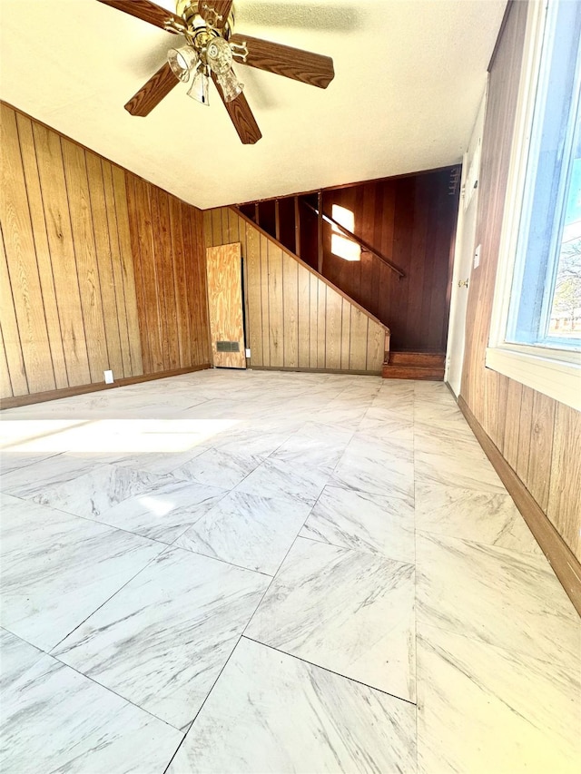 spare room featuring marble finish floor, ceiling fan, and wooden walls