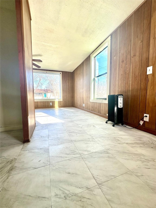 empty room featuring a textured ceiling, wood walls, and baseboards