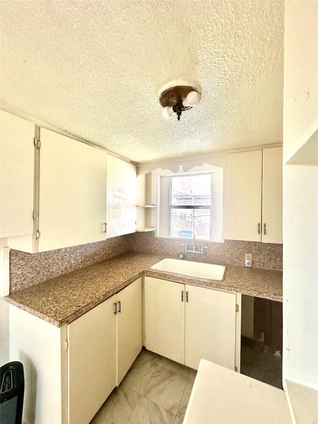 kitchen featuring a textured ceiling, a sink, white cabinets, light countertops, and open shelves