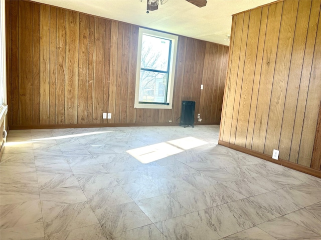 spare room featuring wood walls, radiator heating unit, baseboards, and a ceiling fan