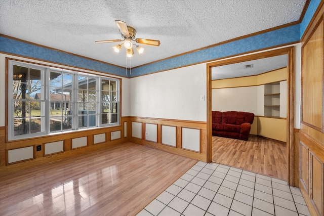 unfurnished room featuring a textured ceiling, wainscoting, and light wood-style flooring