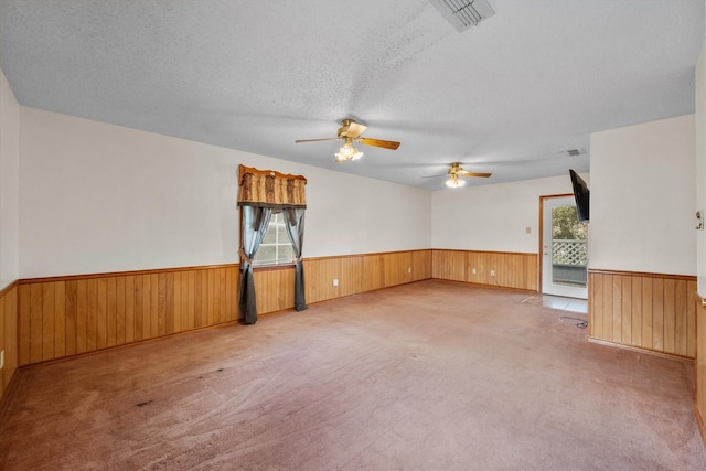 empty room featuring carpet floors, a wainscoted wall, a textured ceiling, and wood walls