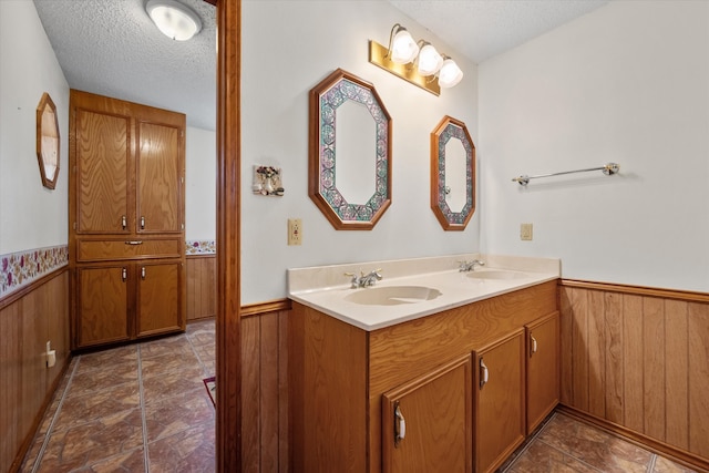 bathroom featuring a wainscoted wall, wooden walls, a textured ceiling, and a sink