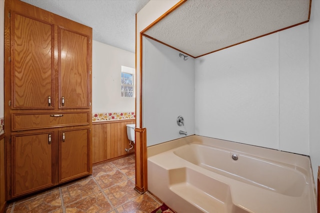 bathroom featuring wooden walls, wainscoting, a textured ceiling, and a bath