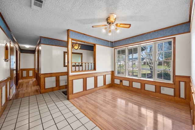 spare room featuring crown molding, wainscoting, visible vents, and light wood-style floors