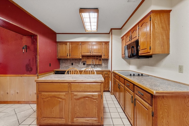 kitchen featuring a center island, a wainscoted wall, ornamental molding, a sink, and black appliances