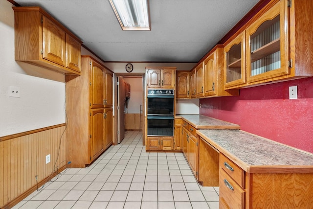 kitchen with glass insert cabinets, built in study area, dobule oven black, and brown cabinets