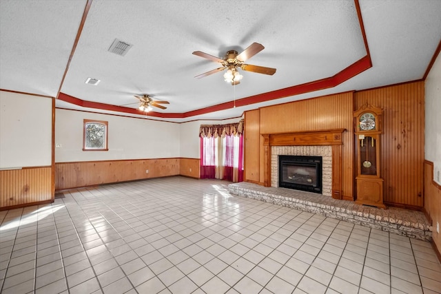 unfurnished living room with a wainscoted wall, wooden walls, visible vents, and a textured ceiling