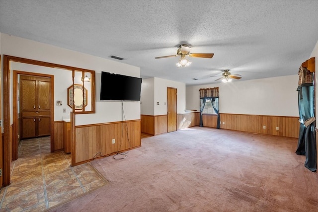 unfurnished living room with a textured ceiling, light carpet, wood walls, visible vents, and wainscoting