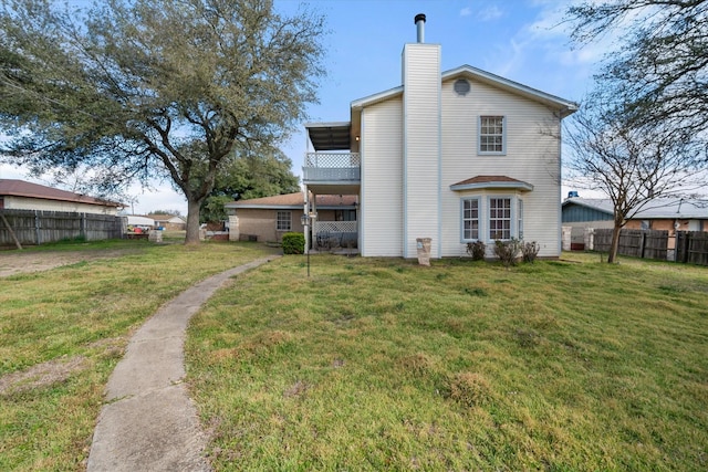 rear view of house featuring a chimney, fence, and a lawn