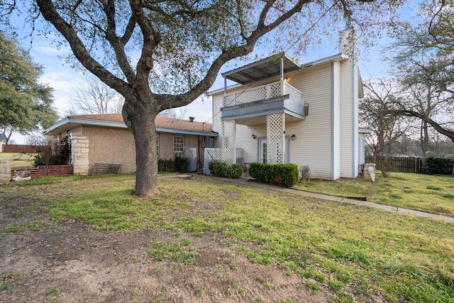 view of front facade featuring a balcony, a chimney, fence, and a front yard