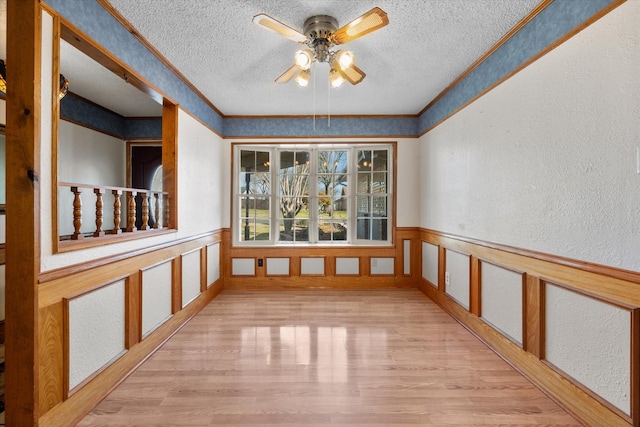 empty room featuring a wainscoted wall, a textured ceiling, wood finished floors, and a textured wall