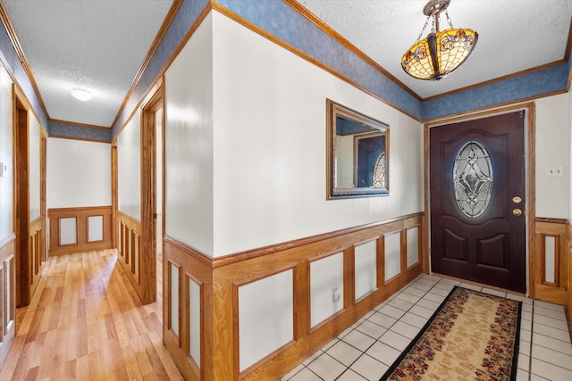 foyer entrance featuring a textured ceiling, a wainscoted wall, and crown molding