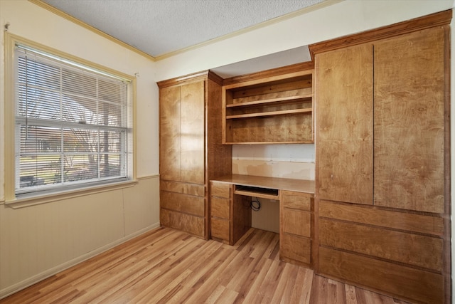 unfurnished office with a textured ceiling, built in desk, light wood finished floors, and crown molding