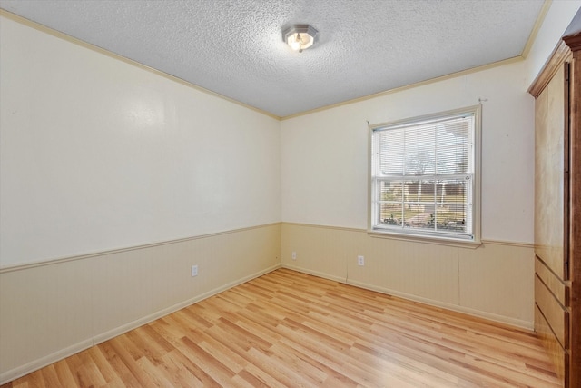 spare room with light wood-type flooring, wainscoting, crown molding, and a textured ceiling